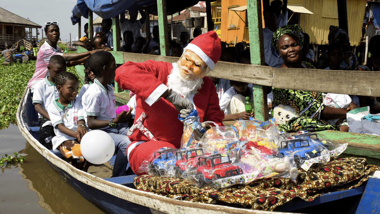 Un hombre vestido de Papá Noel se prepara para distribuir regalos durante su recorrido en el pueblo palafito de Ganvié antes de las celebraciones navideñas en Cotonú, Benín
